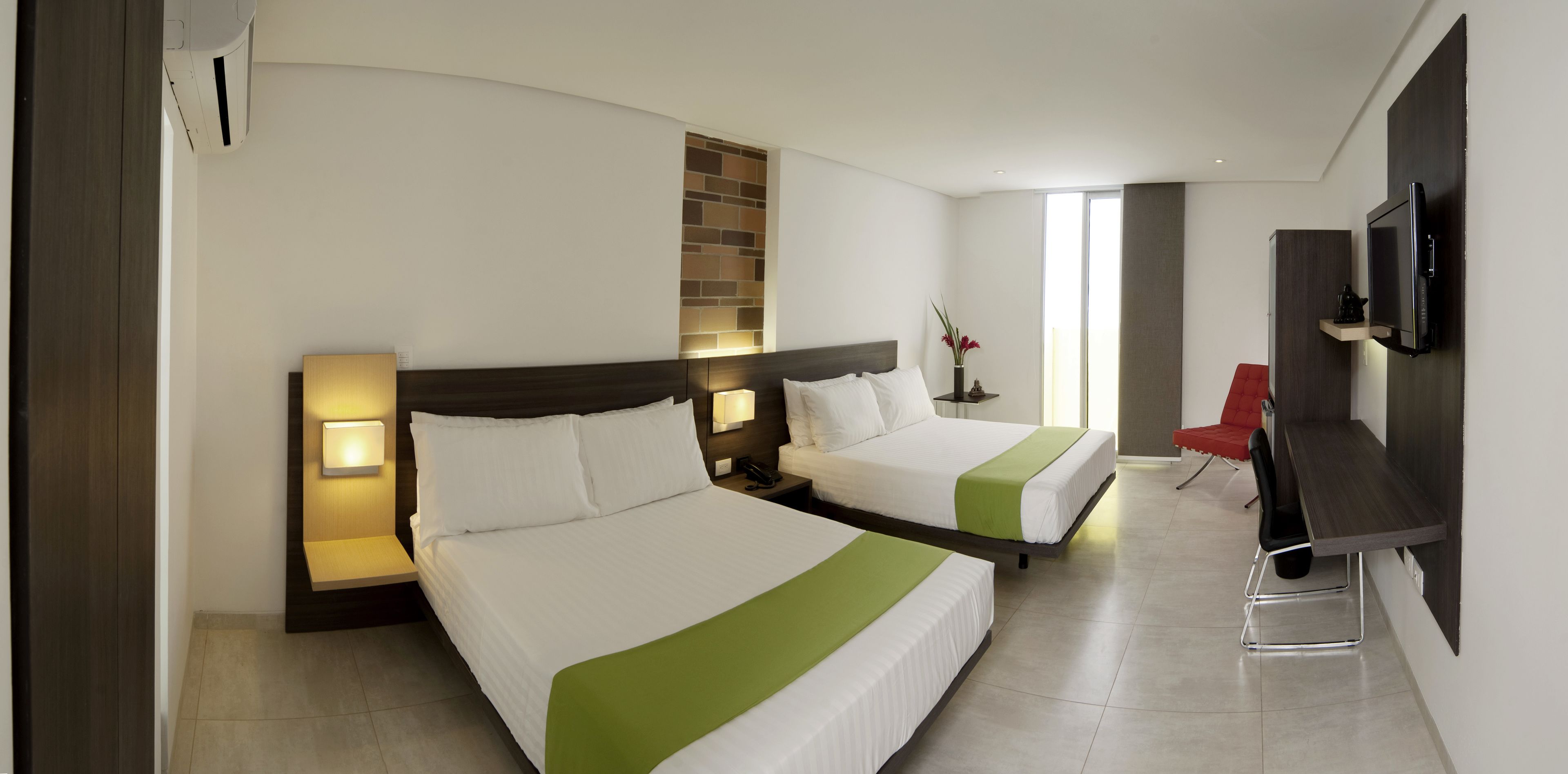 Habitación de hotel con dos camas, un escritorio, un televisor y una silla roja.