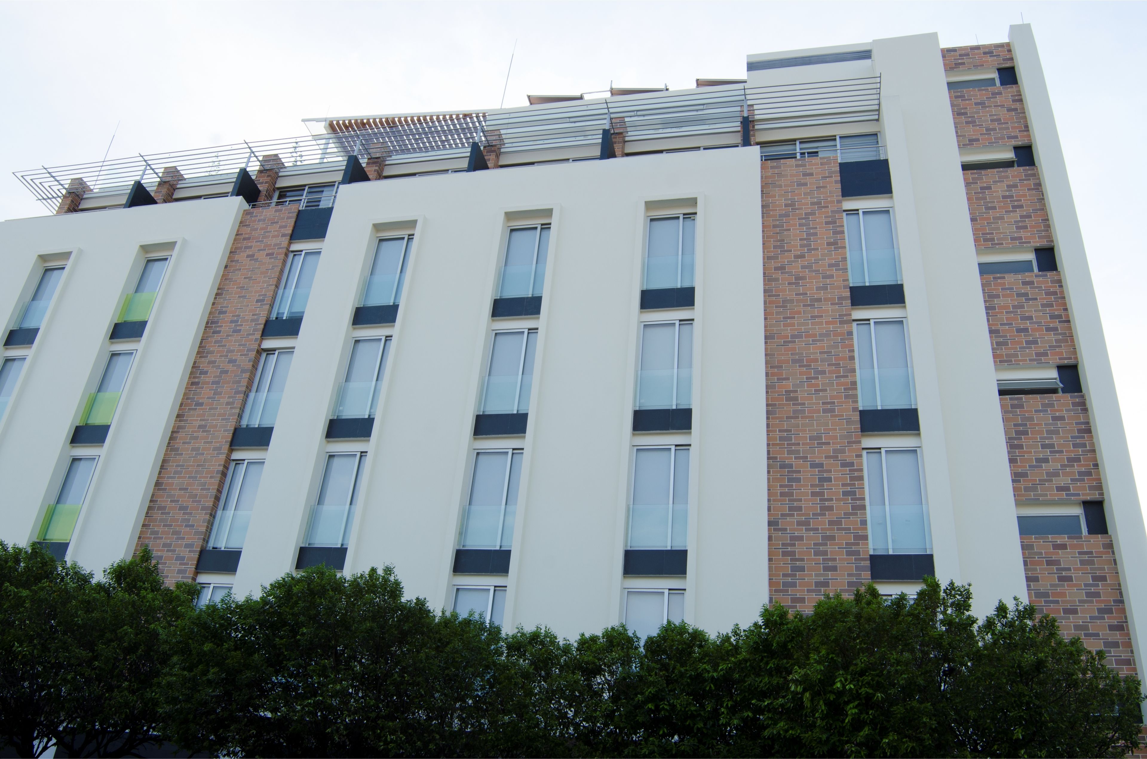 A multi-story building with a modern architectural design, featuring a combination of brick and white exterior walls, large windows, and a flat roof with solar panels.