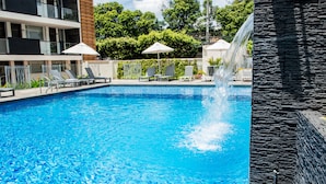 A swimming pool with lounge chairs and umbrellas, a waterfall feature, and a stone wall. - Hotel Casa Blanca (San José de Cúcuta)