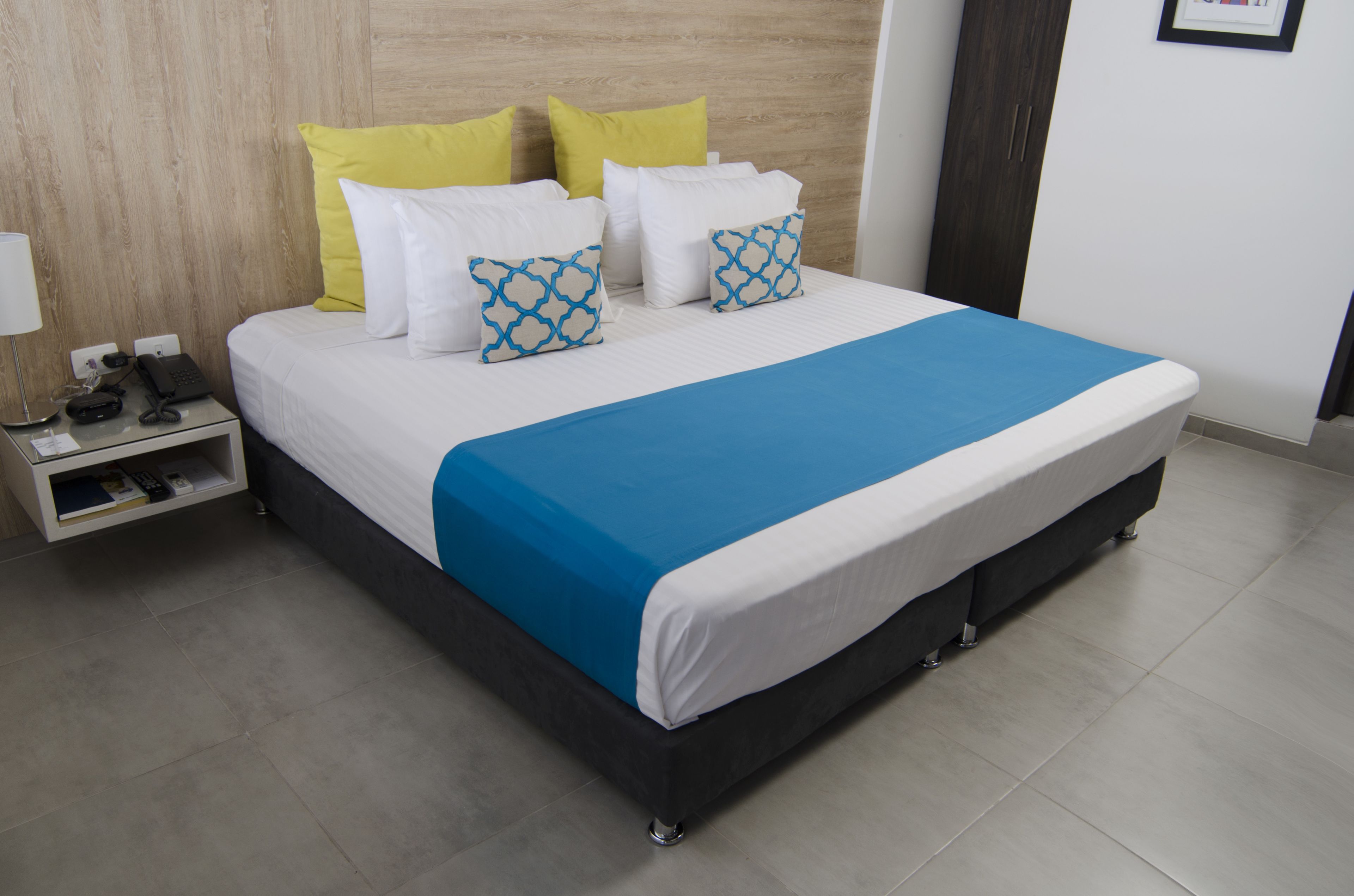 A neatly made bed with a blue and white bedspread, two yellow pillows, and two patterned pillows.