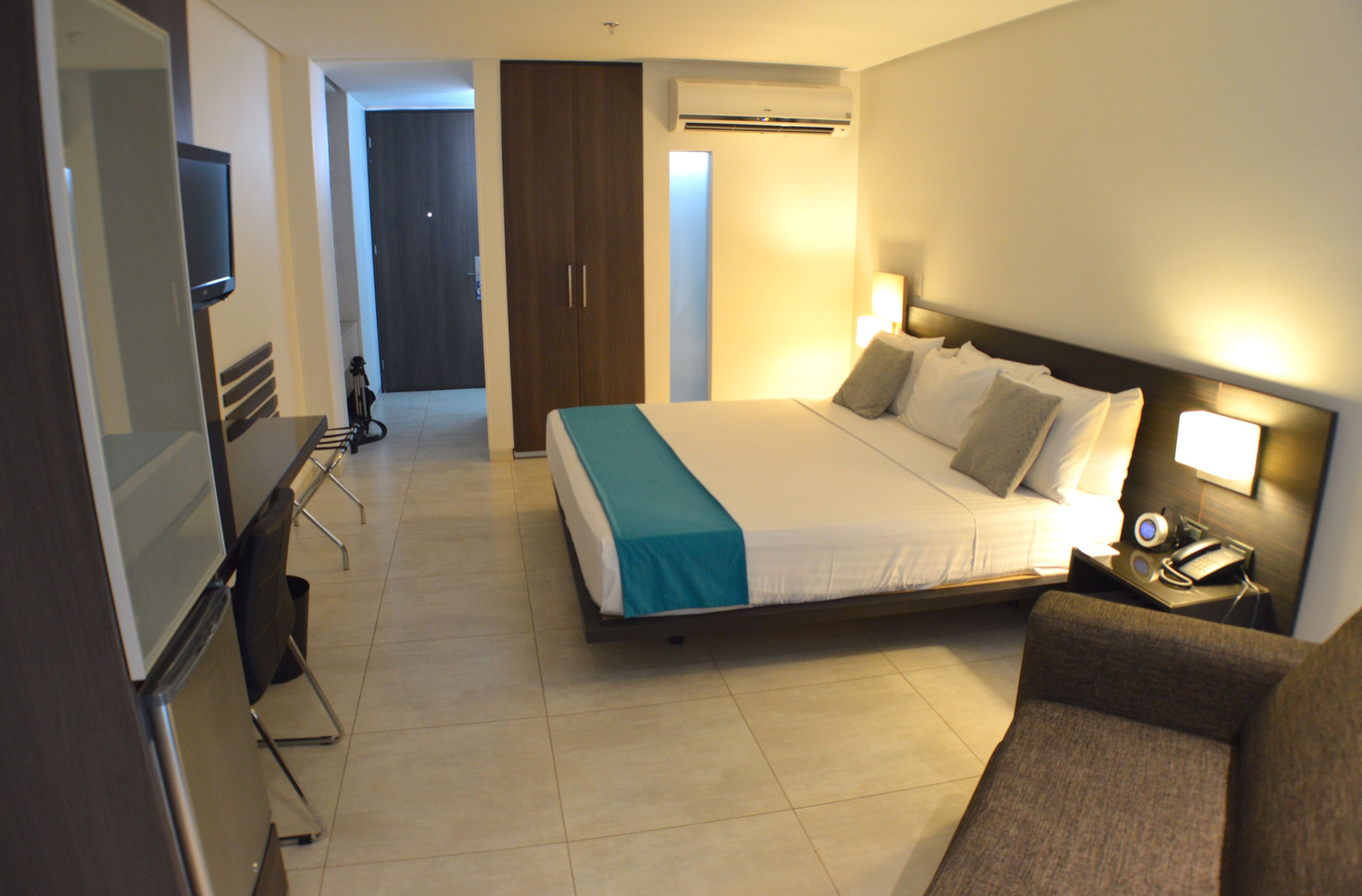A hotel room with a bed, bedside table, lamp, and a TV on a stand.
