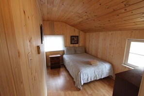 A small, wooden-paneled bedroom with a single bed, a nightstand, and a window.