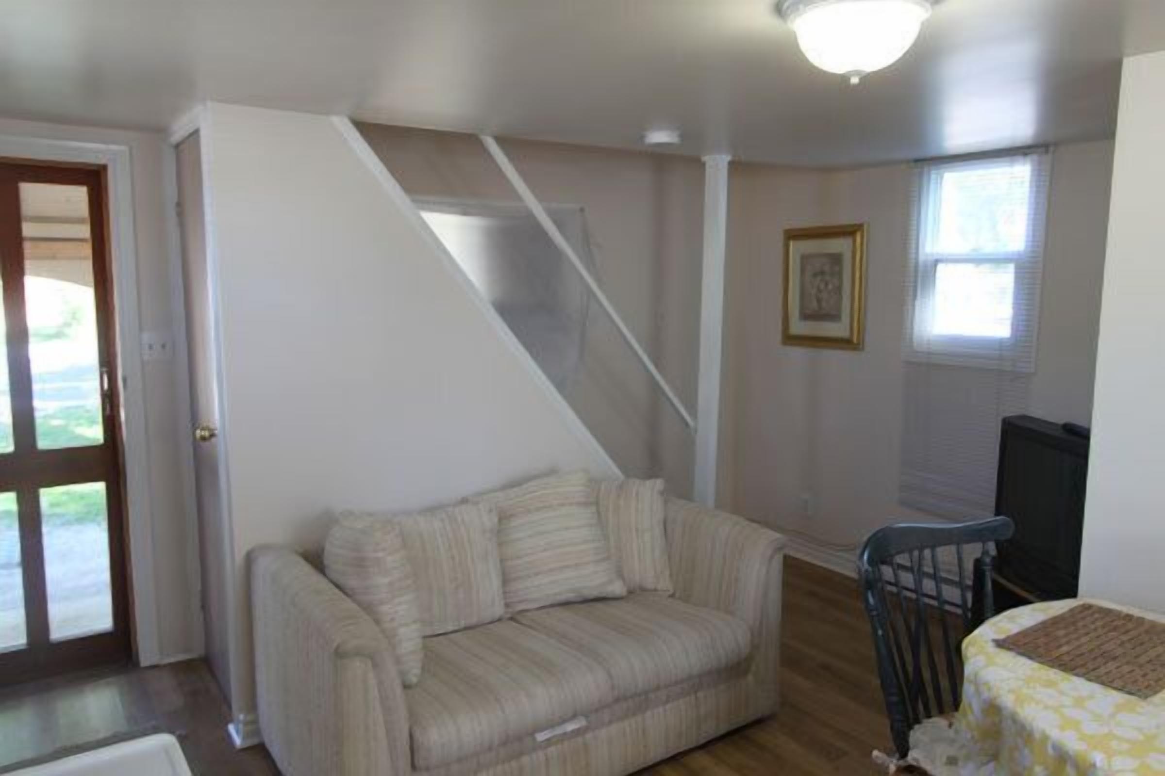 A living room with a sofa, a dining table with a chair, a staircase, and a framed picture on the wall.