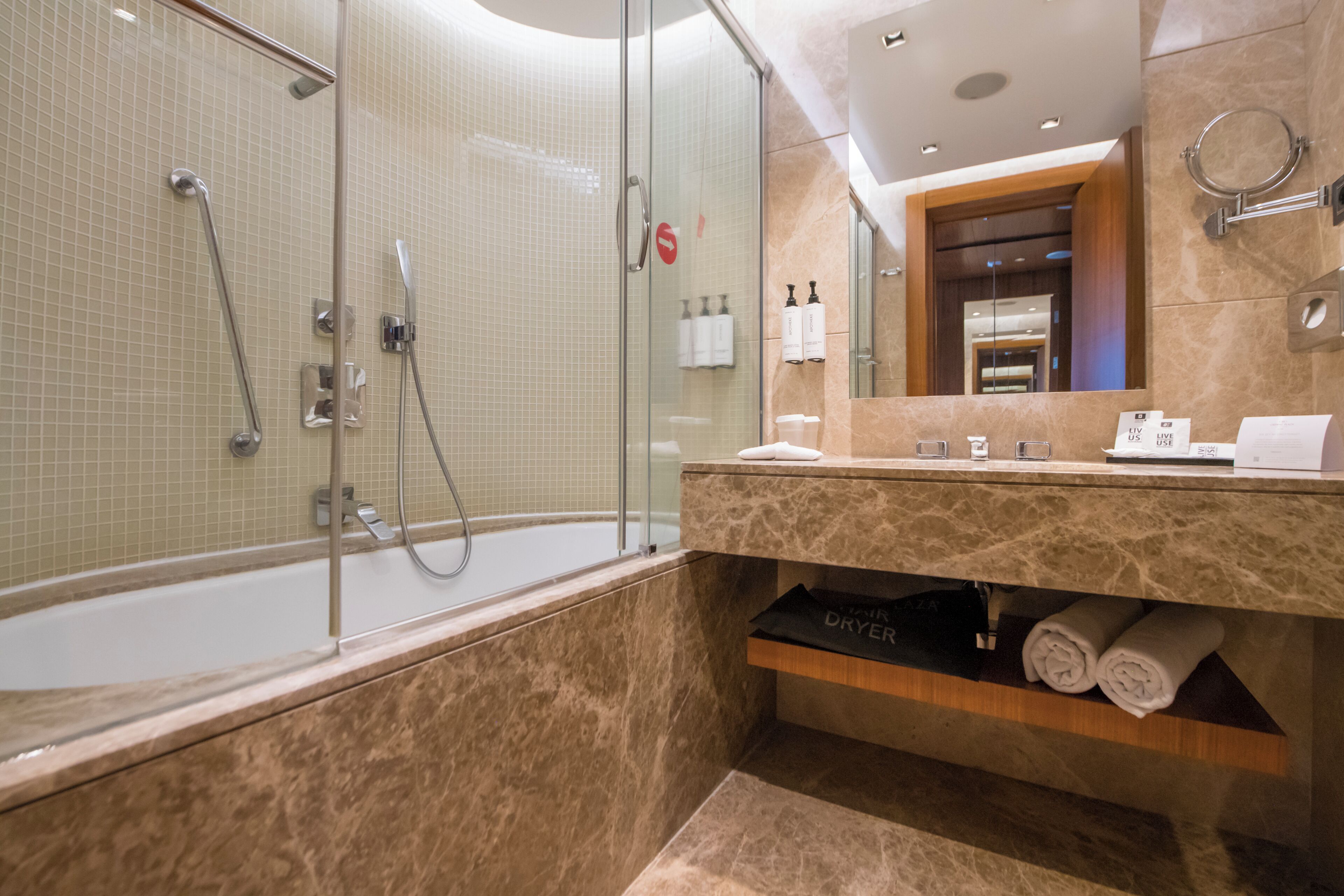 Une salle de bain moderne avec une douche à parois de verre, un meuble-lavabo en marbre et des serviettes soigneusement pliées.