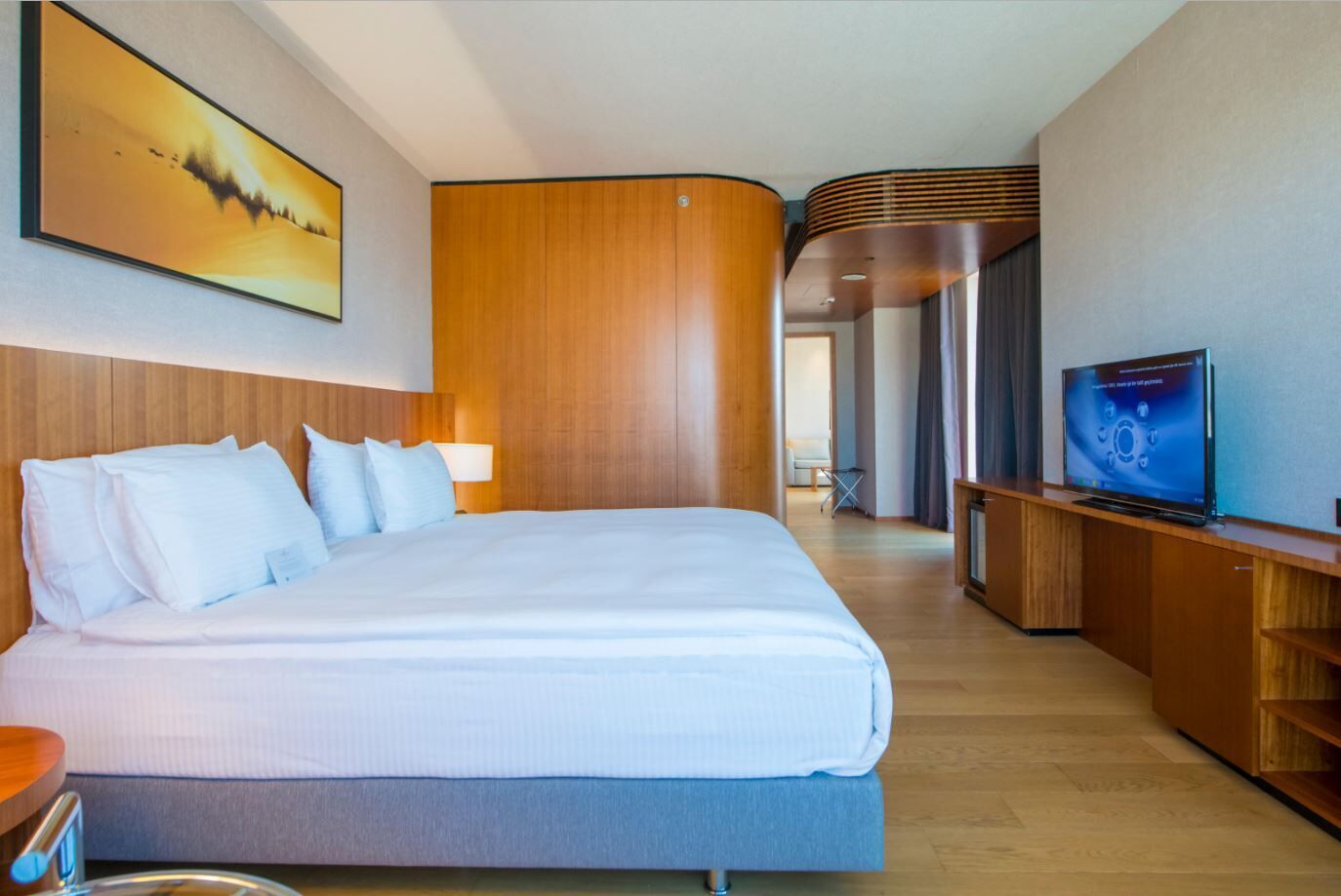 A hotel room with a large bed, a television, and a painting on the wall.