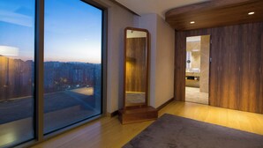 A modern hotel room with a large window, a wooden floor, a mirror, and a door leading to another room. - Crowne Plaza Kayseri by IHG (Kayseri)
