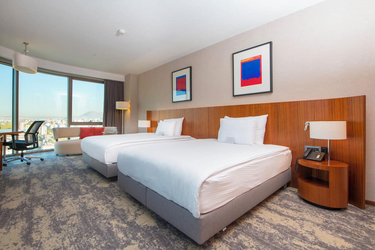 Habitación de hotel con una cama grande, un escritorio y una silla. Hay dos cuadros en la pared, una lámpara en el escritorio y un teléfono en la mesita de noche.