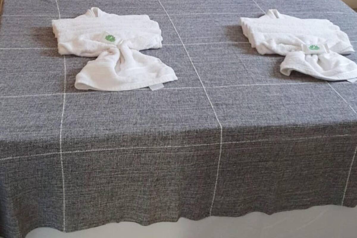 A bed with white pillows, a gray blanket, and folded towels on the bed.