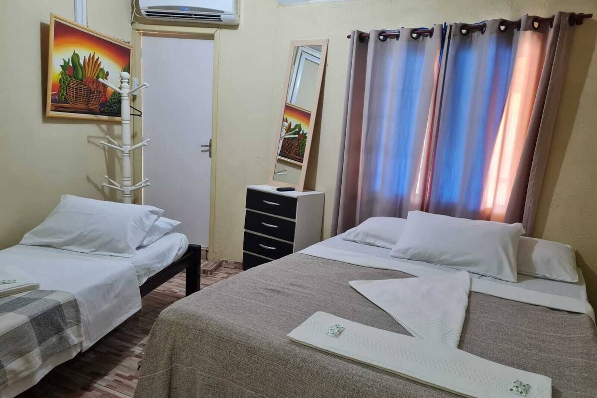 A hotel room with two single beds, a dresser, a mirror, and a painting of fruits.