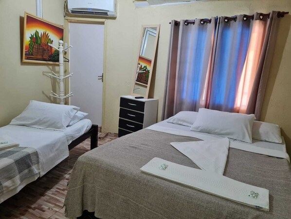 Une chambre d’hôtel avec deux lits simples, une commode, un miroir et un tableau représentant des fruits.