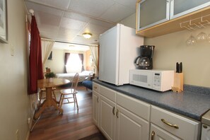 A compact kitchen with a refrigerator, microwave, and coffee maker. There is a dining area with a table and chairs.