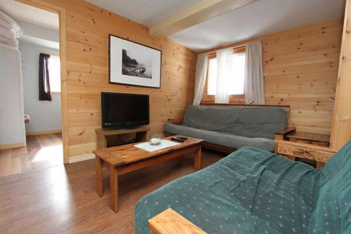 Una habitación acogedora con detalles de madera, un sofá, un televisor y una ventana con cortinas.