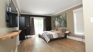 A bedroom with a bed, a TV mounted on the wall, a window with curtains, and a painting on the wall. - Beachfront Beach Houses (Wasaga Beach)