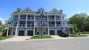 A multi-story residential building with balconies, a garage, and a car parked in front. - Beachfront Beach Houses (Wasaga Beach)