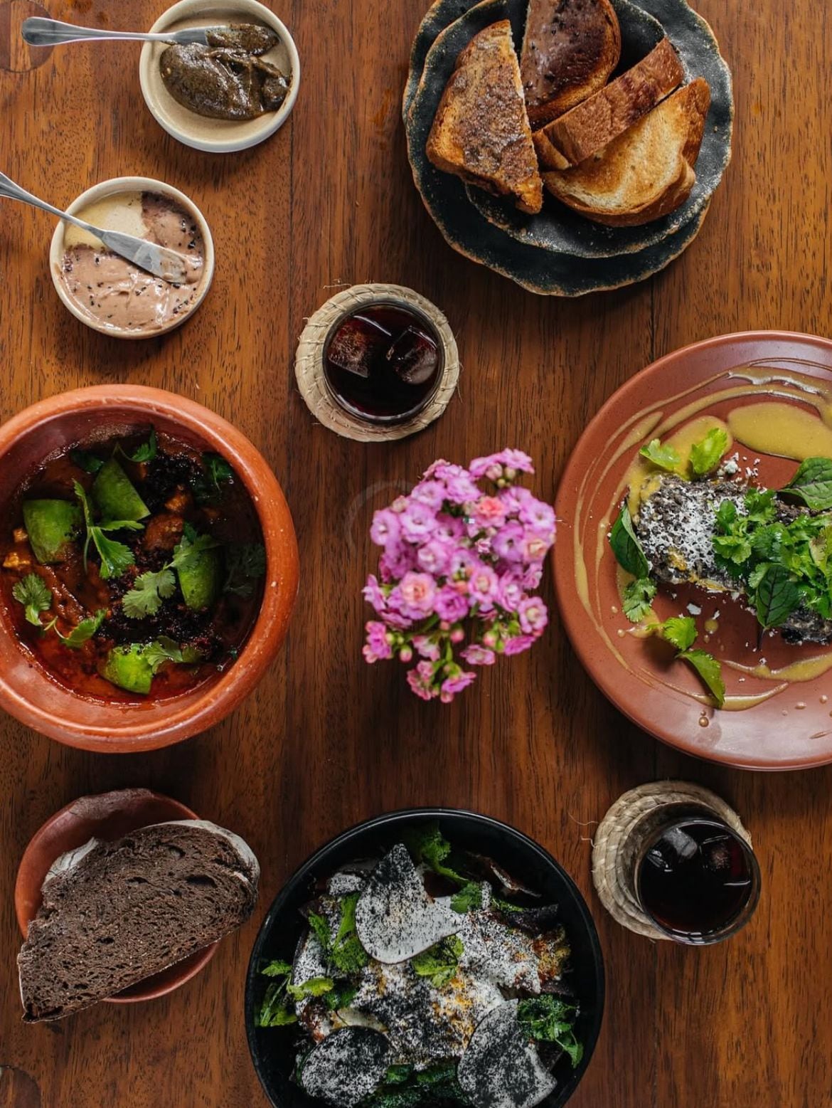 Une table en bois sur laquelle on trouve différents plats, notamment du pain, un bol de soupe et une assiette de légumes verts et de fromage.