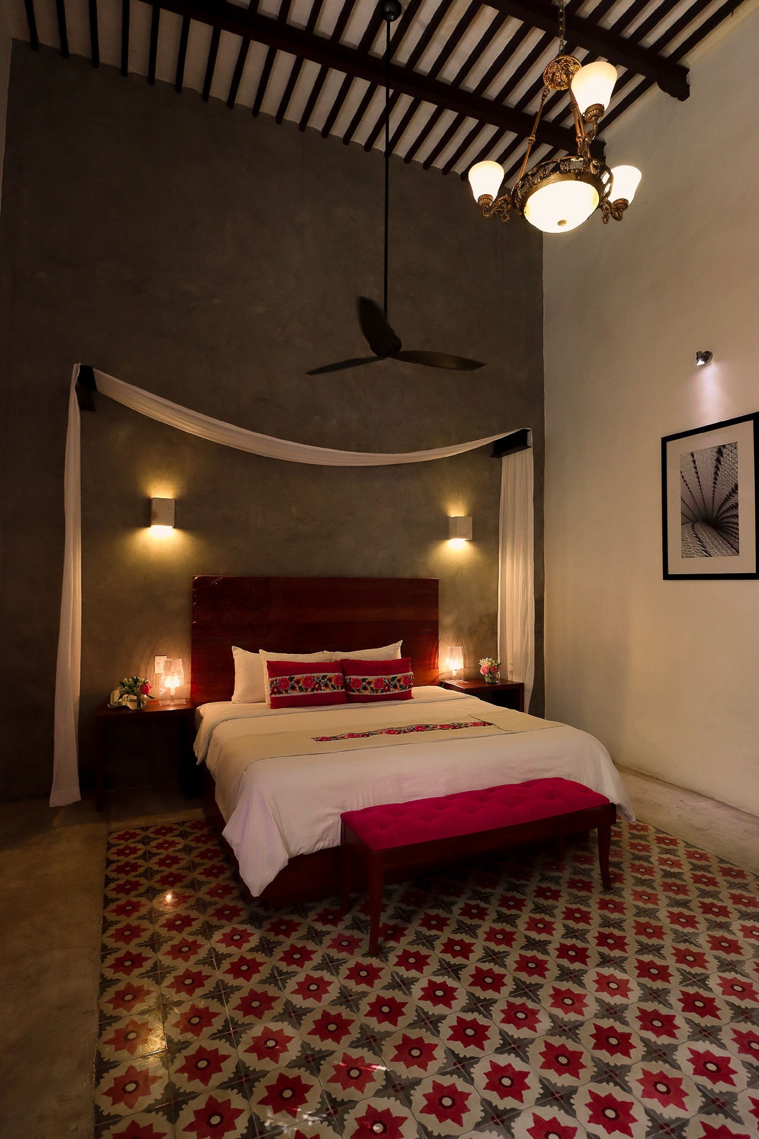 A bedroom with a canopy bed, a ceiling fan, patterned floor tiles, and a chandelier.