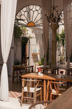 Un área de patio al aire libre con mesas y sillas de madera, un candelabro decorativo de hierro forjado y vistas del jardín circundante.