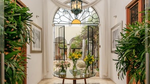 A glass-top table with vases of flowers in a hallway with a tiled floor and wooden doors. - Casa de Las Palomas by Palomas Hotels -  Adults only (Mérida)