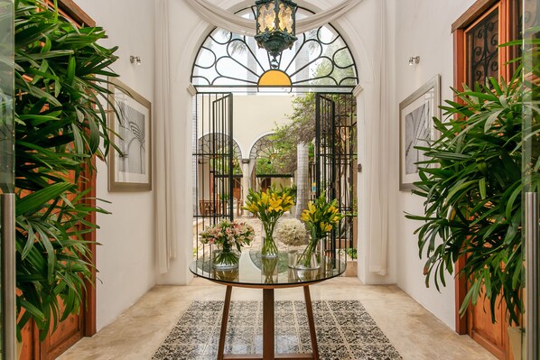 Una mesa con cubierta de vidrio y jarrones de flores en un pasillo con piso de baldosas y puertas de madera.