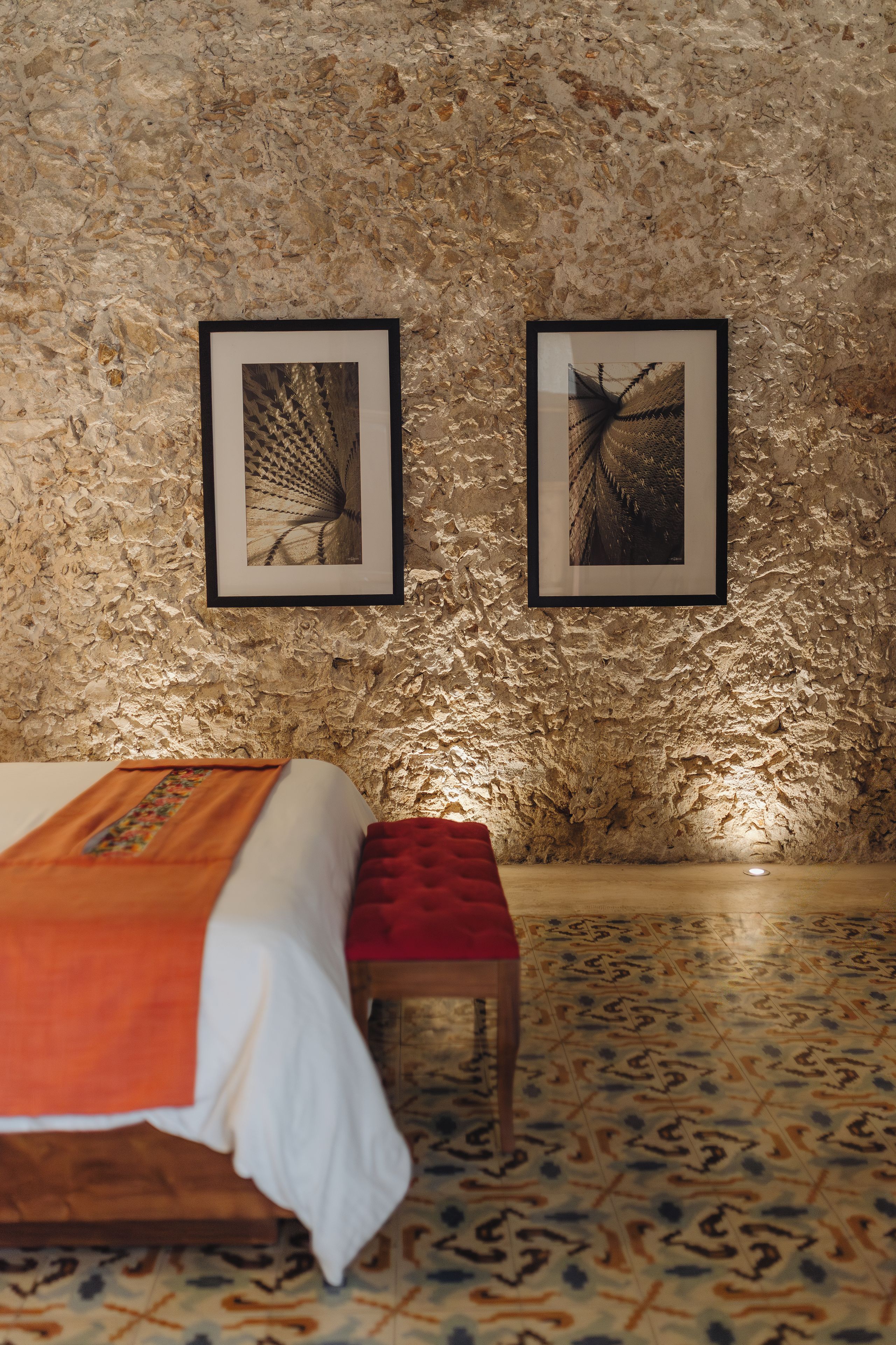A room with a bed, a bench, and two framed pictures on the wall.