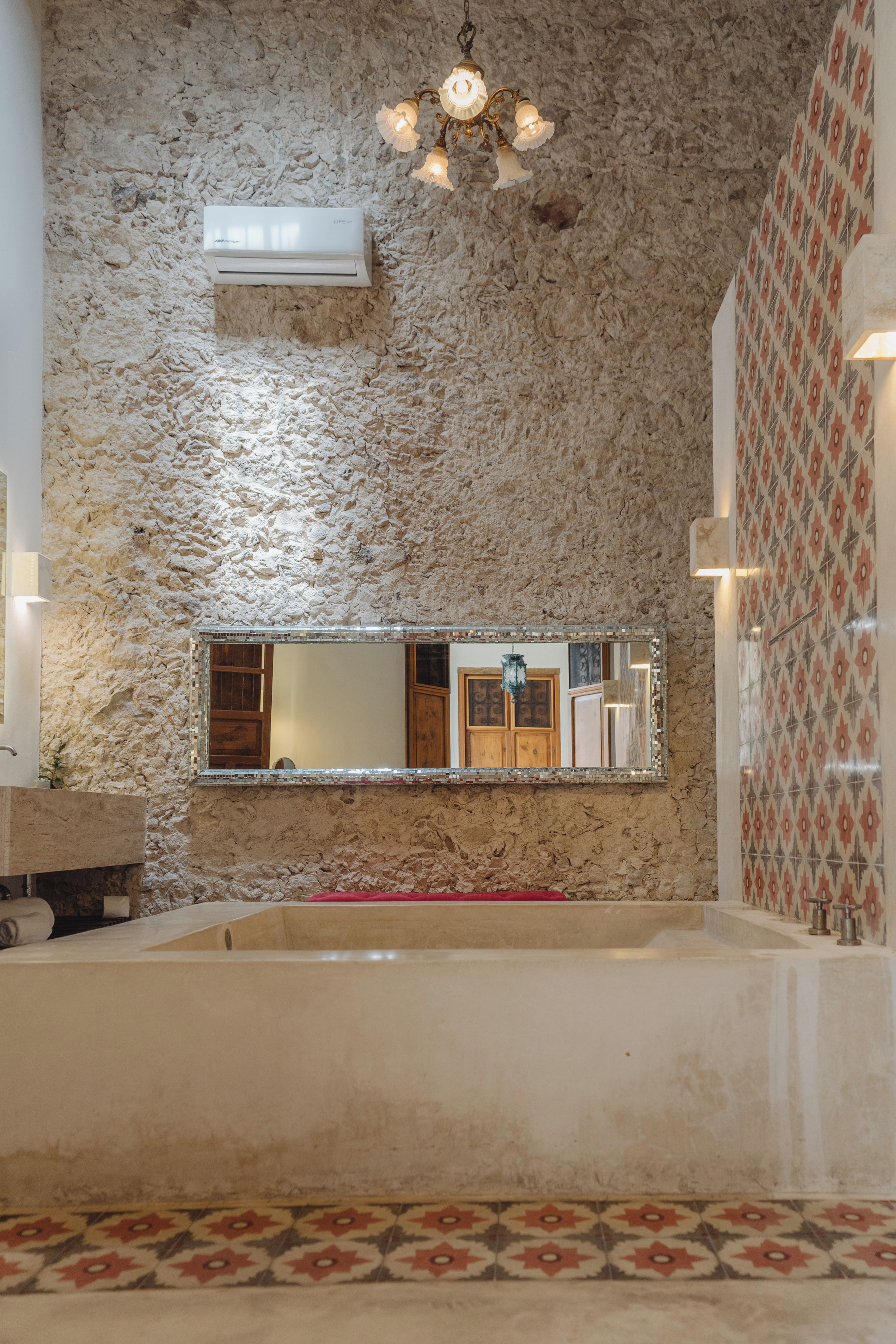 A bathroom with a stone wall, a large mirror, a bathtub, and a patterned wall.