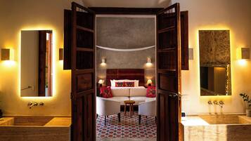 A hotel room with a large bed, two bedside tables, a small round table, and a bathroom with a bathtub and sink.