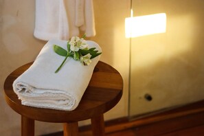 A neatly folded white towel with a small floral arrangement on a wooden stool in a room with a white wall and a visible light switch. - Casa de Las Palomas by Palomas Hotels -  Adults only (Mérida)