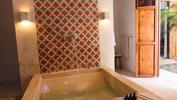 A spa area with a large bathtub, decorative wall tiles, and a wooden door leading to another room.