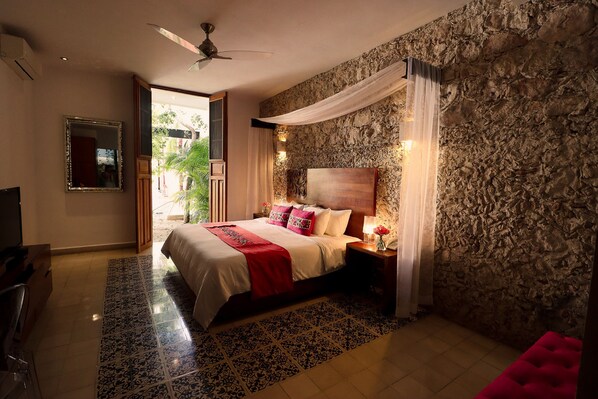 A bedroom with a bed, nightstand, lamp, and a stone wall. - Casa de Las Palomas by Palomas Hotels -  Adults only (Mérida)