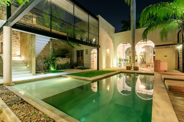Un edificio moderno con piscina, mobiliario exterior y una escalera que lleva a un nivel superior.