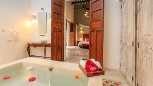 A bathroom with a bathtub, a sink, and a mirror. There is a wooden door leading to a bedroom. - Casa de Las Palomas by Palomas Hotels -  Adults only (Mérida)