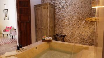 Un baño con una bañera grande, un armario de madera y una pared de piedra.