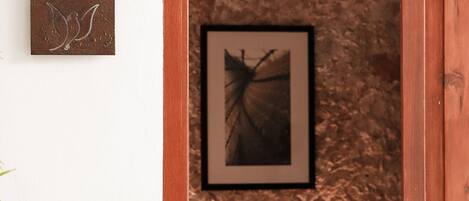 Un pasillo estrecho con una pared texturizada, un cuadro enmarcado y una silla roja.