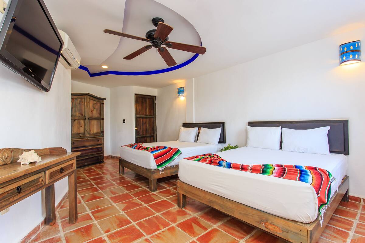 Habitación de hotel con dos camas, televisión, ventilador de techo y un mueble de madera.