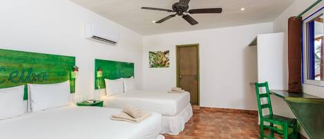 Habitación de hotel con dos camas, ventilador de techo, aire acondicionado, una silla verde y un escritorio.