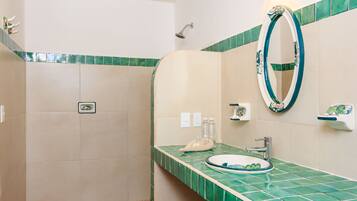 Un baño con ducha, lavamanos con espejo y paredes con azulejos verdes.