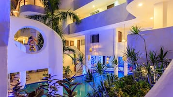 Un hotel de varios niveles con una zona de piscina rodeada de plantas tropicales.