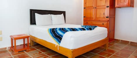 A bed with a white mattress and a blue and white striped blanket, a wooden headboard, a small wooden nightstand, and a wooden wardrobe with a mirror.