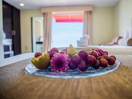 Una bandeja de fruta sobre una mesa con vista a una habitación de hotel al fondo.