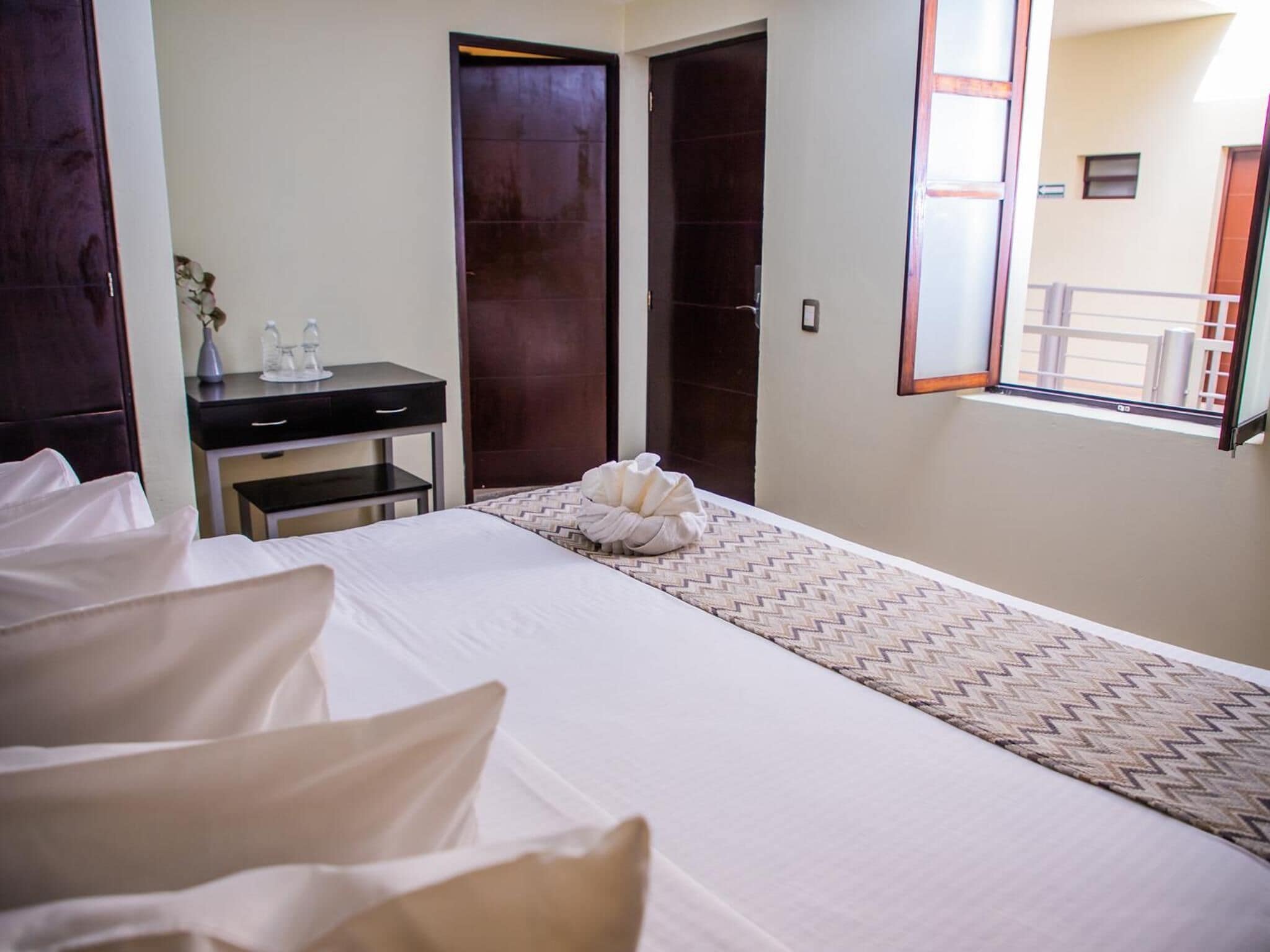 A hotel room with a bed, a desk, a chair, a dresser, and a window with a view of the outside.