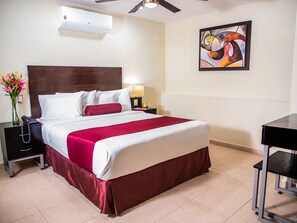 A hotel room with a bed, a nightstand, a desk, an air conditioner, and a painting on the wall. - H177 Hotel (Campeche)