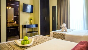 A hotel room with a bed, a TV, a desk with a vase, and a mirror. - H177 Hotel (Campeche)