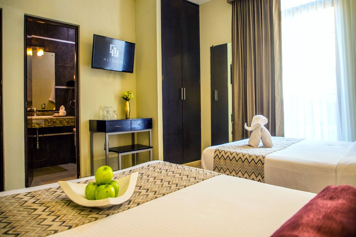 A hotel room with a bed, a TV, a desk with a vase, and a mirror.