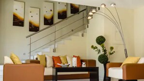A modern living room with a sofa, coffee table, and two armchairs. There is a staircase with a railing and a floor lamp. - H177 Hotel (Campeche)