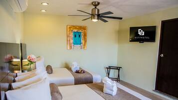 A hotel room with two beds, a ceiling fan, a TV, and a painting on the wall.
