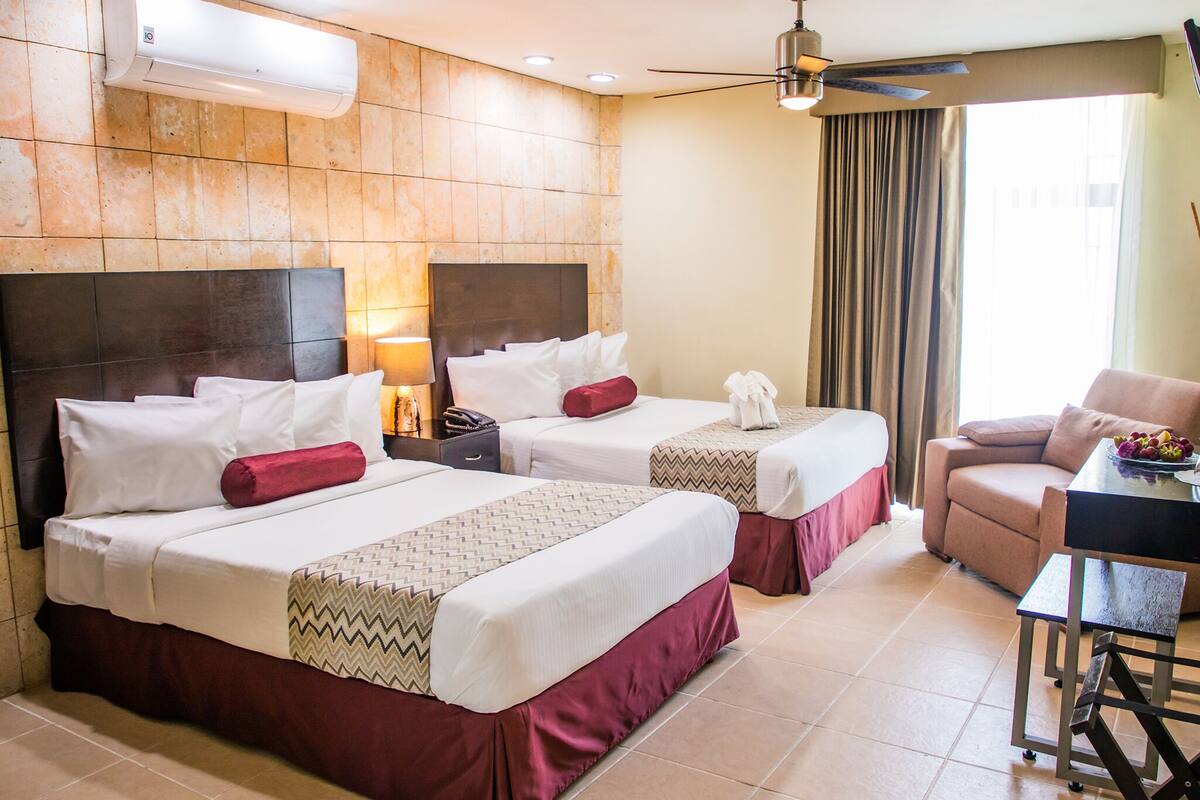 A hotel room with two beds, a desk, a chair, a ceiling fan, and a window with curtains.