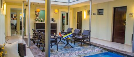 Vestíbulo de hotel con zona de piscina, mobiliario y un mostrador de recepción.