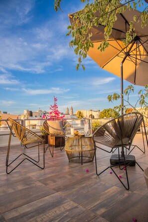 Terraza en la azotea con sillas de mimbre, una mesa y una planta en maceta.
