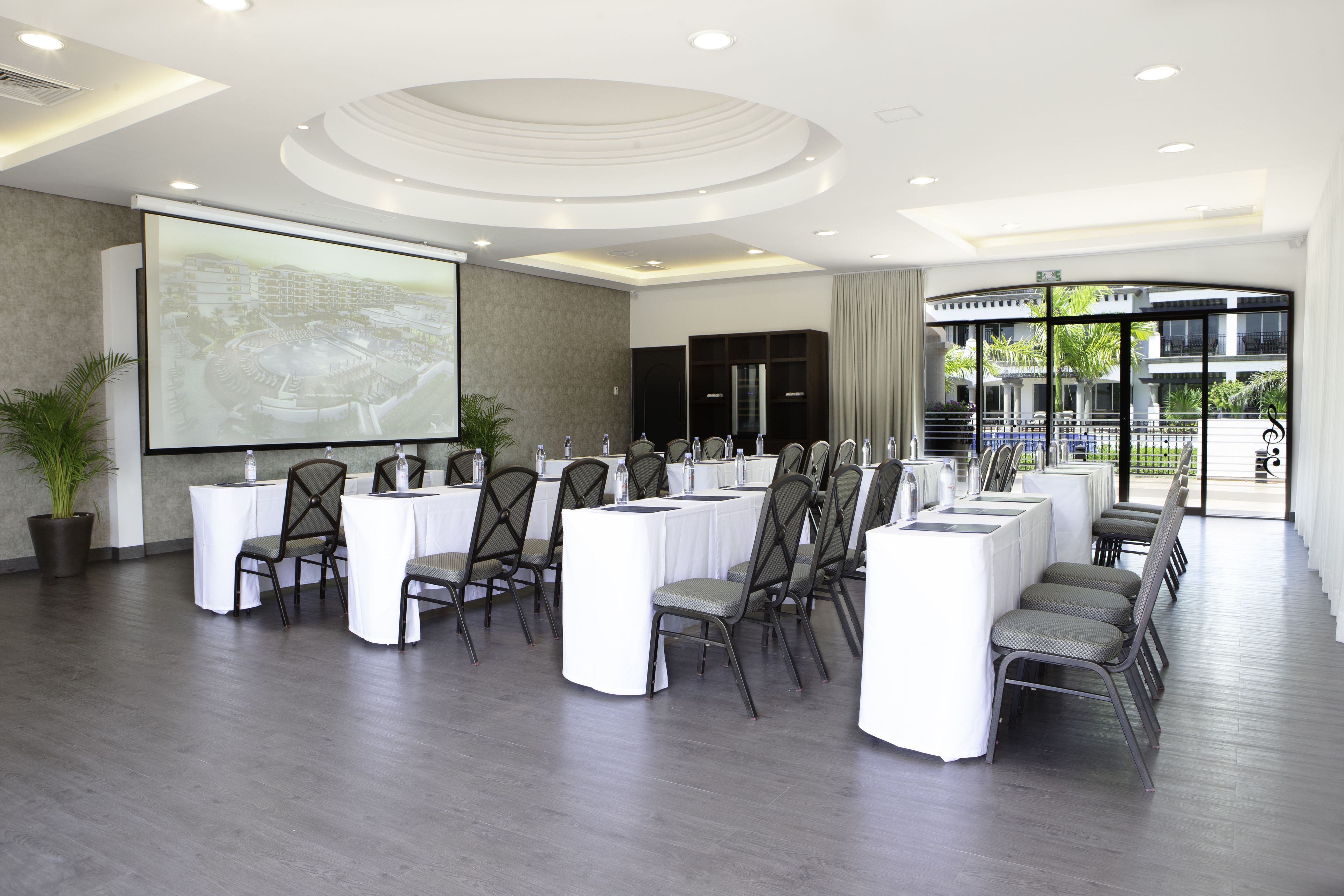 A conference room with a large screen, white tables, and chairs arranged for a meeting.