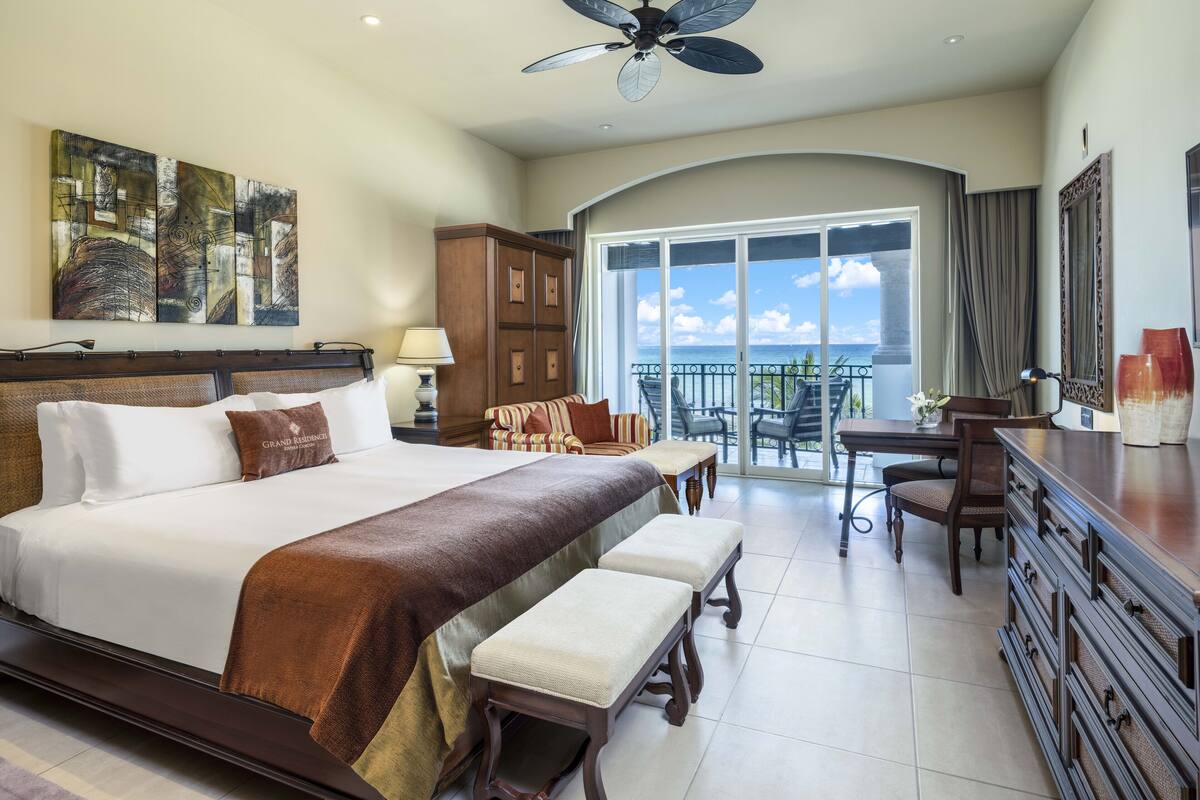 A spacious hotel room with a large bed, a balcony with a view, and a dining area.